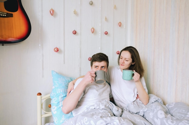 happy young couple, family. Beautiful woman, handsome man relaxing in modern bedroom in bed, kissing