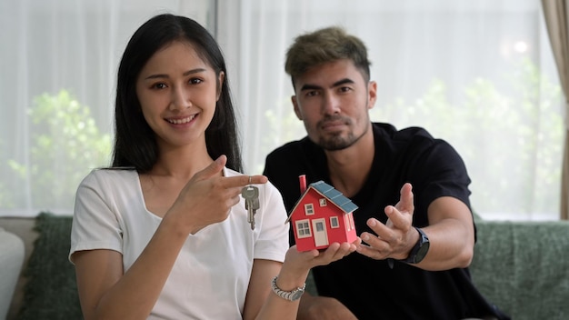 Happy young couple holding house model and smiling to camera New house insurance and real estate concept