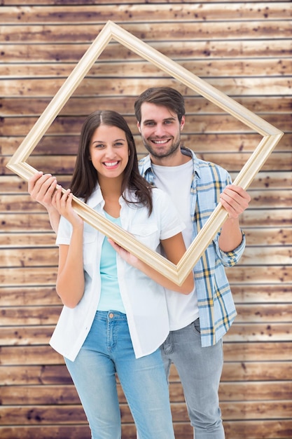 Happy young couple holding picture frame against wooden planks