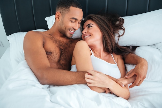 Happy young couple lying in bed and looking at each other