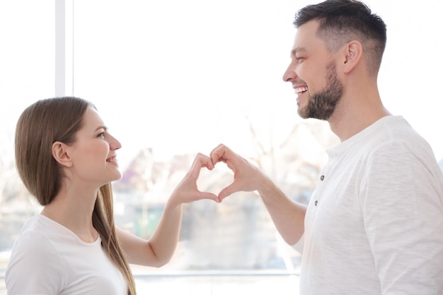 Happy young couple making heart with their hands at home