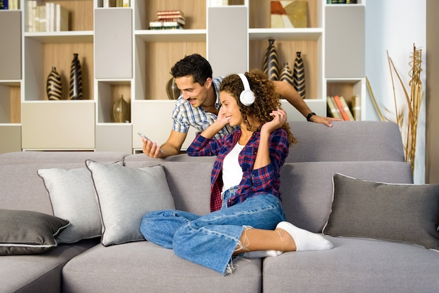 Happy young couple relaxing choosing music together on a mobile phone in the living room enjoying some quality time