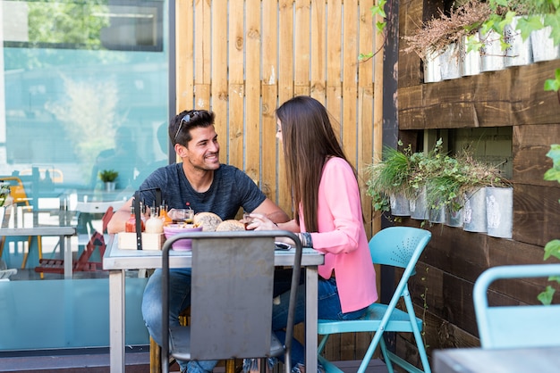 Happy young couple seating in a restaurant terrace eating a burger