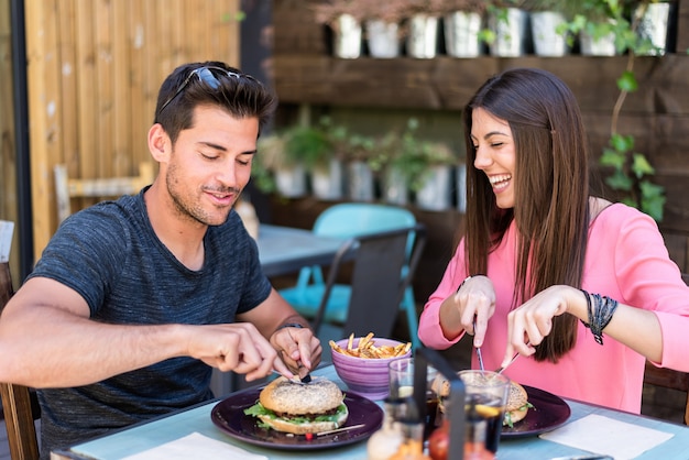 Happy young couple seating in a restaurant terrace eating a burger