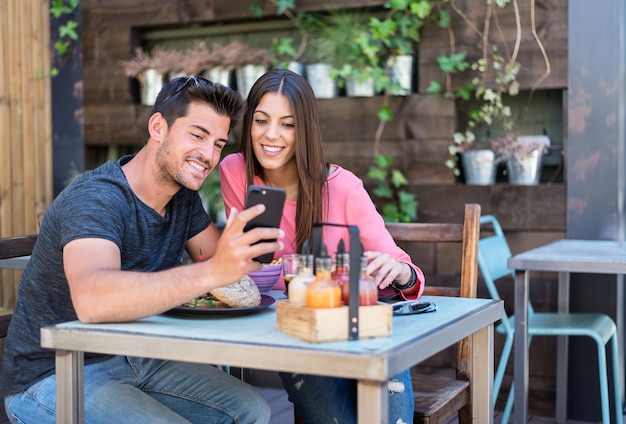 Happy young couple seating in a restaurant terrace with a smartphone