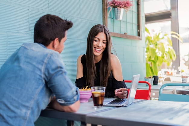 Happy young couple seating in a restaurant with a laptop