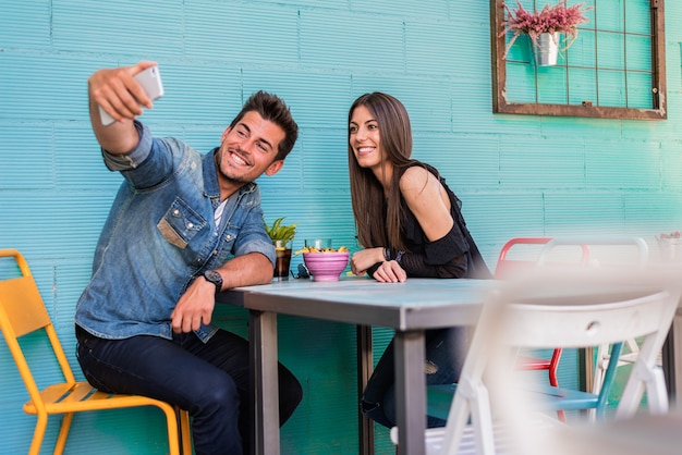 Happy young couple seating in a restaurant with a smartphone taking a selfie