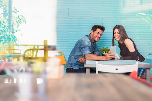 Happy young couple seating in a restaurant with a smartphone