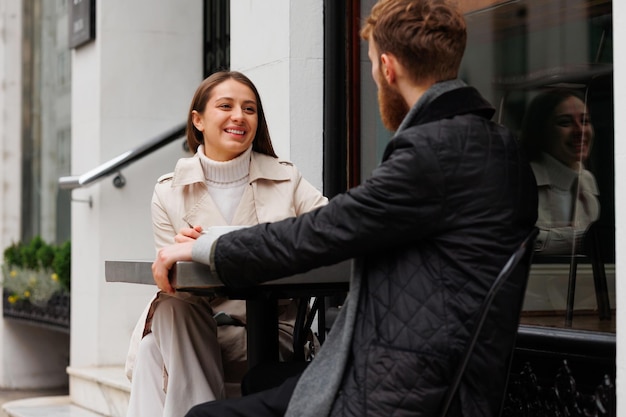 Happy young couple sitting at cafe table on London street talking and laughing