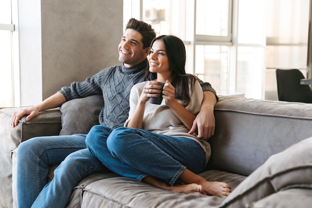 Happy young couple sitting on a couch at home, watching TV