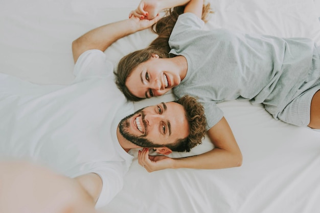 Happy young couple taking selfie portrait with smart mobile phone lying on bed