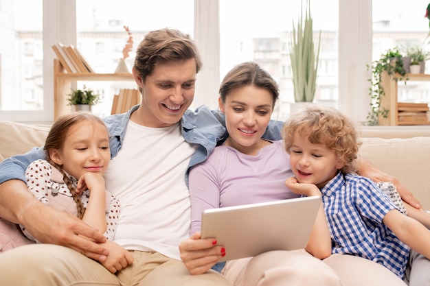 Happy young couple and their two kids in casualwear relaxing together on couch