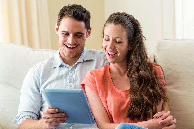 Happy young couple using digital tablet on sofa in living room