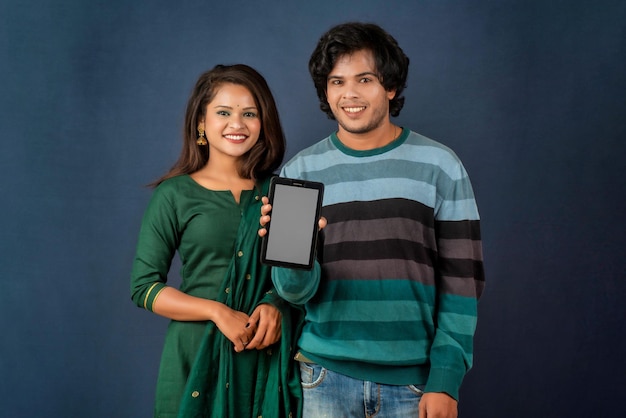 Happy young couple using mobile and showing a blank screen of a smartphone or mobile or tablet phone on a gray background