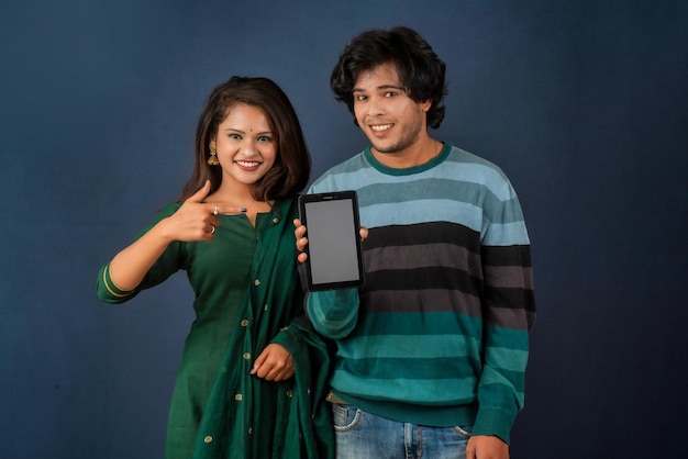 Happy young couple using mobile and showing a blank screen of a smartphone or mobile or tablet phone on a gray background