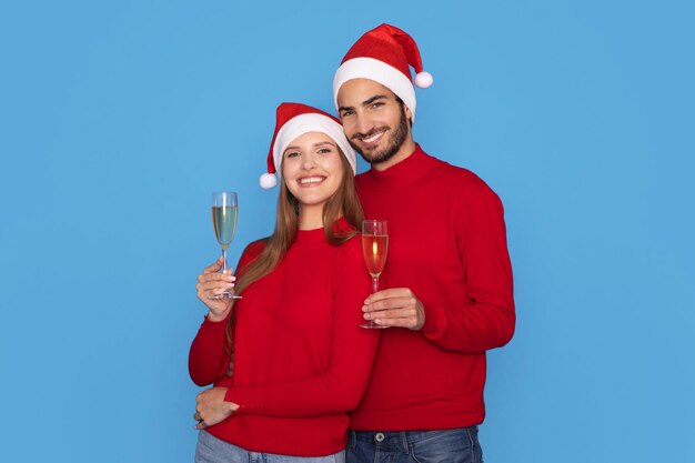 Photo happy young couple wearing santa holding champagne glasses and smiling at camera