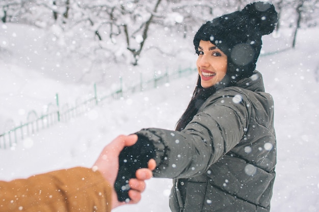 Happy Young Couple in Winter . Family Outdoors. man and woman looking upwards and laughing. Love, fun, season and people - walking in winter park. Stand and hold each other's hands