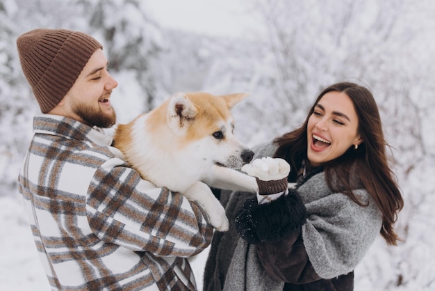 Happy young couple with akita dog in forest on winter and snowly day