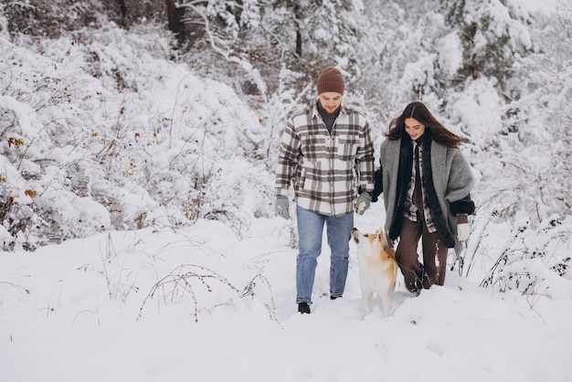 Happy young couple with akita dog in forest on winter and snowly day