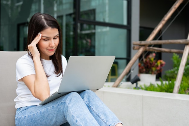 Happy young entrepreneur woman sitting on tanning bed beside pool and using laptop computer