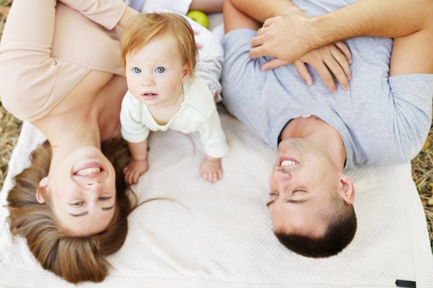 Happy young family spending time together, mother and father with baby outside in green nature.