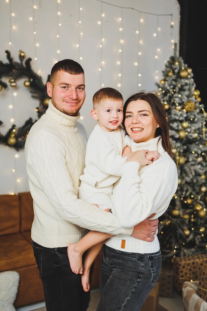 A happy young family with a small child is celebrating the New Year at home near the Christmas tree Christmas with the family New Year time to celebrate