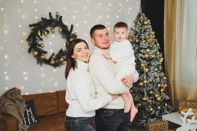 A happy young family with a small child is celebrating the New Year at home near the Christmas tree Christmas with the family New Year time to celebrate