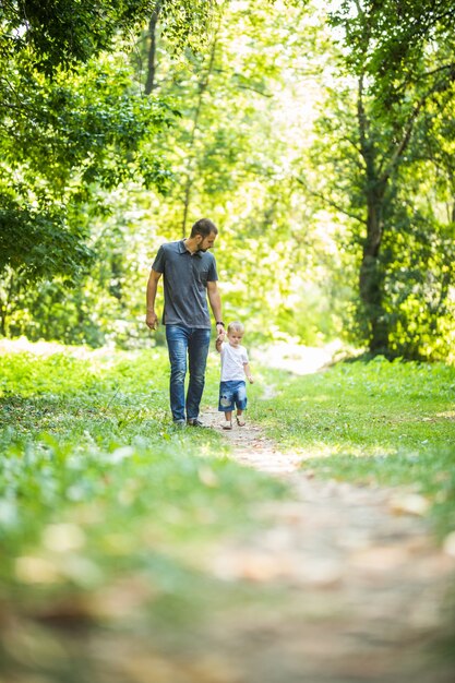 Happy young father holding his little son by hand and walking on the park