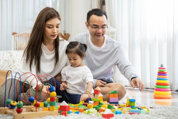 Happy young father and mother and a little daughter playing with Toy wooden blocks, sitting on the floor in living room, family, parenthood and people concept with Developmental toys