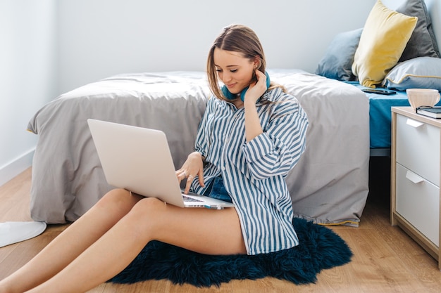 happy young female siting in her bedroom browsing on notebook while listening to music