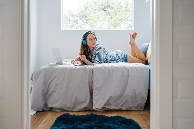 happy young female siting in her bedroom browsing on smart phone while listening to music