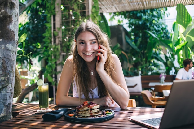 Happy young female talking on phone during breakfast