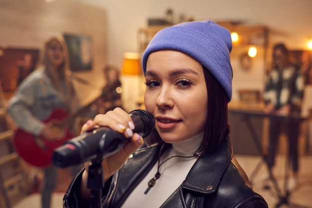 Happy young female with microphone looking at you while singing