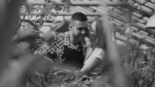 Happy young florist couple in apron working in greenhouse