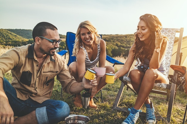 Happy young friends enjoy a sunny day in nature. They're cooking tea, laughing and talking happy to be together.