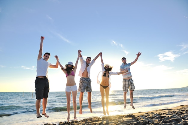 happy young friends group have fun and celebrate while jumping and running on the beach at the sunset