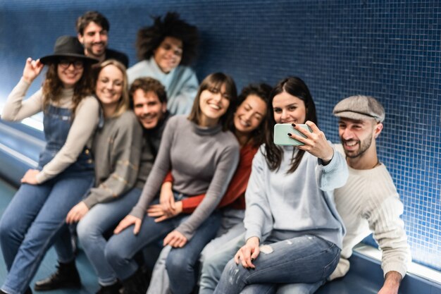 Photo happy young friends having fun doing selfie in metro subway station - focus on hand holding mobile phone