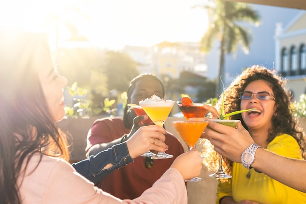 Happy young friends having fun outside and toasting with cocktails together Focus on the glasses