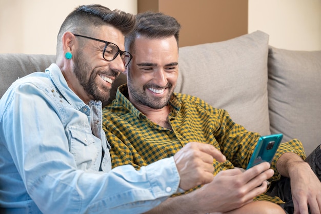 Happy young gay couple using mobile phone while sitting on a sofa in the living room