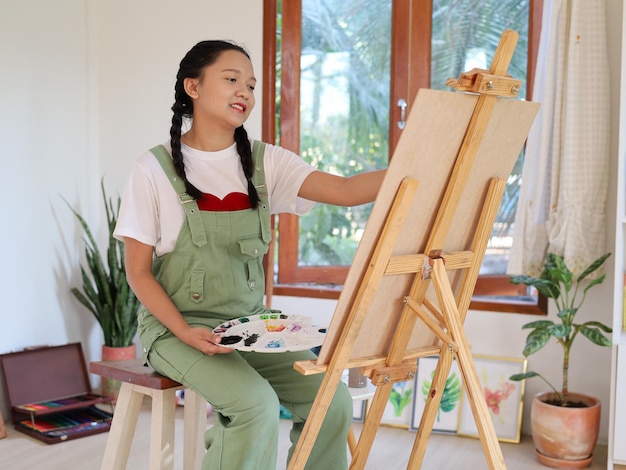 Happy young girl drawing with a paint palette and a paintbrush at home painting artist