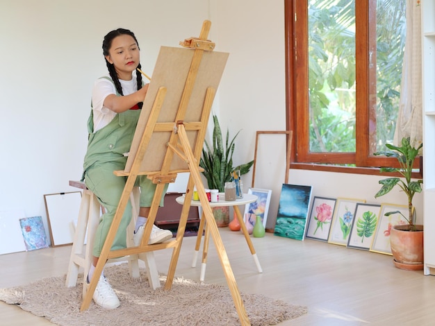 Happy young girl drawing with a paint palette and a paintbrush at home painting artist