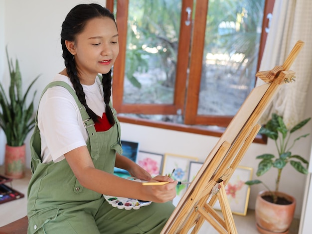 Happy young girl drawing with a paint palette and a paintbrush at homepainting artist