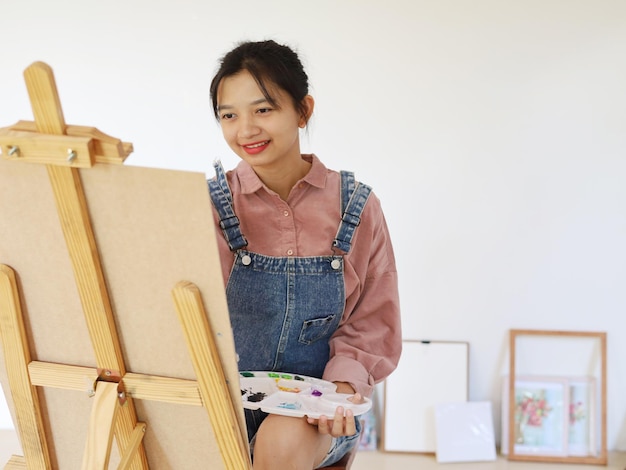 Happy young girl drawing with a paint palette and a paintbrush at homepainting artist