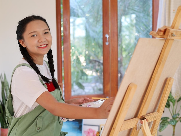 Happy young girl drawing with a paint palette and a paintbrush at homepainting artist