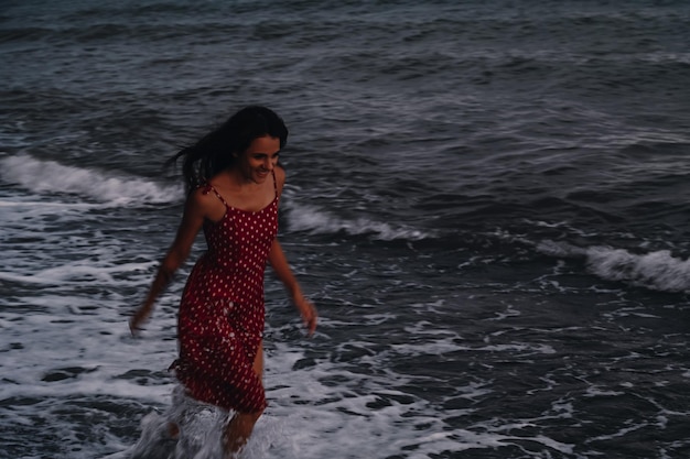 A happy young girl in a dress runs along the sea waves on the beach on a summer evening