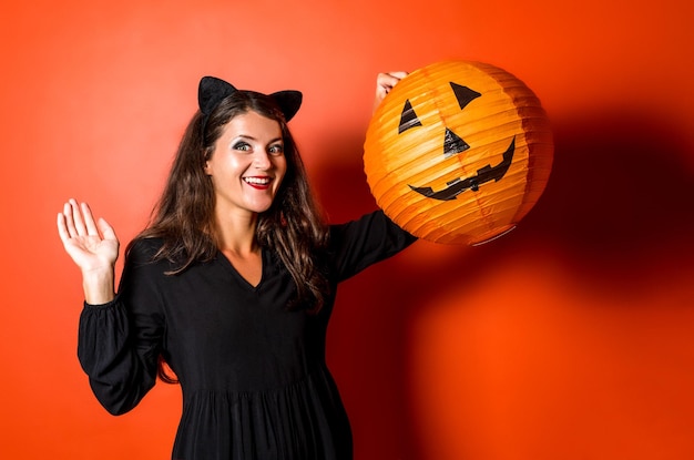 Photo happy young girl in halloween costume holding big pumpkin lantern