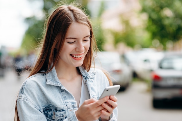 Happy young girl  holding a smartphone standing and smiling outdoor