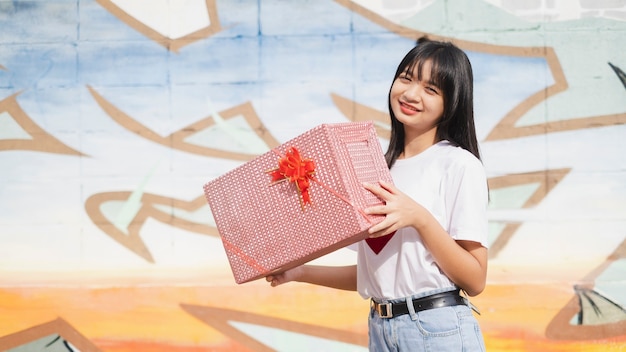 Happy young girl holds the present box on colorful background. Asian young girl.