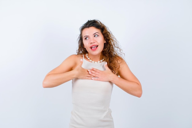 Happy young girl is looking right and putting hands on chest on white background