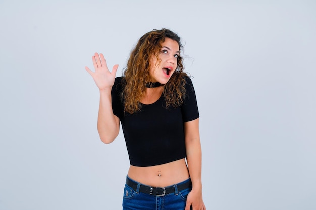 Happy young girl is looking up by showing hi gesture on white background